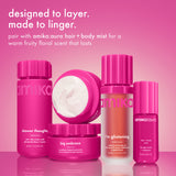 amika's body wash, body cream, and aura hair and body mist are grouped together on a pink background. text reads “designed to layer. made to linger,” with a note about pairing for a warm fruity floral scent.